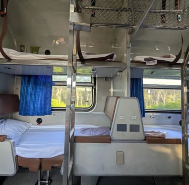 Interior of a sleeper train cabin featuring multi-level bunk beds with white linens and blue curtains.