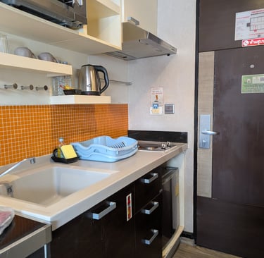 Modern studio kitchenette featuring an orange tile backsplash, microwave, and electric kettle.