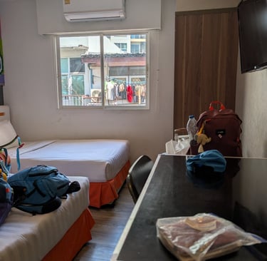 A budget hostel room with twin beds, air conditioning, and a view of a city window.