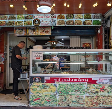 A local Thai street food stall in Bangkok featuring a colorful menu display of traditional curry and stir-fry dishes.