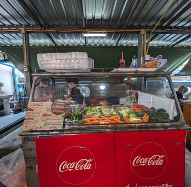 Street food vendor in Thailand preparing fresh fruit smoothies and juices at a Coca-Cola branded market stall.