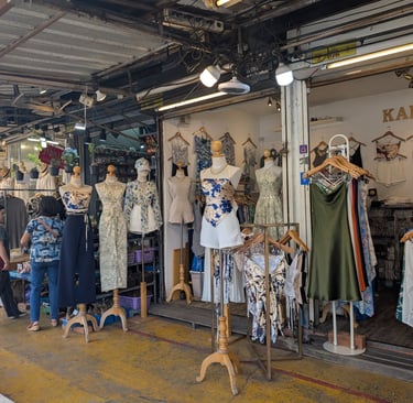 A women's clothing boutique in a market featuring floral dresses and stylish outfits on mannequins.