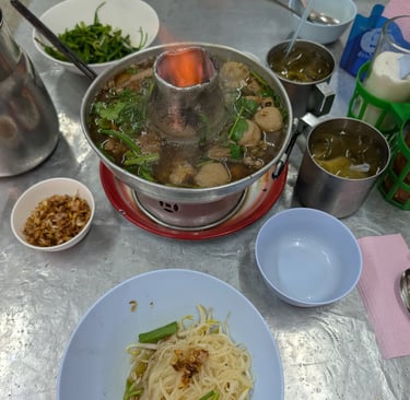 Authentic Thai beef hot pot with meatballs and noodles served on a street food table with a live flame.