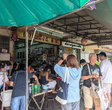 Diners eat at a busy authentic Thai street food stall under a green umbrella in Bangkok.