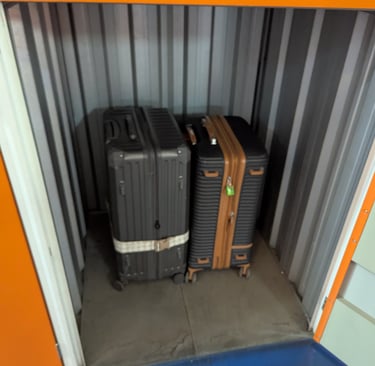 Two hardside suitcases stored inside a secure metal self-storage unit with orange trim.