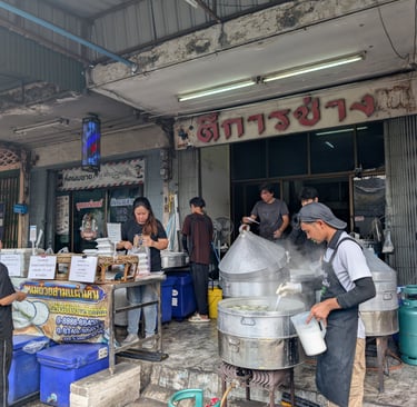Street food vendors preparing steamed dishes in large metal pots at an authentic Thai food stall.