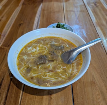 Traditional Myanmar fish curry soup served in a white bowl on a rustic wooden table.