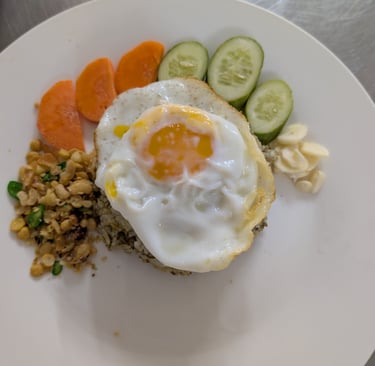 A plate of savory tearice topped with a sunny-side-up egg, served with sliced cucumbers and carrots.