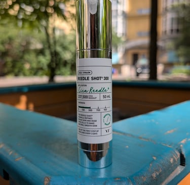 A bottle of VT Cosmetics Reedle Shot 300 facial essence sits on a blue wooden ledge outdoors.