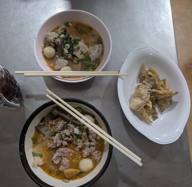 Two bowls of Thai pork noodle soup with fish balls and a side of crispy fried fish skin.