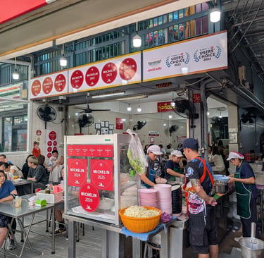 Diners eat at an open-air Michelin Guide street food stall in Bangkok featuring red award stickers.