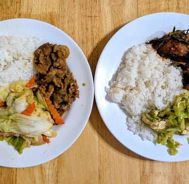 Two plates of Thai food with white rice, stir-fried cabbage, beef, and spicy fish curry on a wooden table.