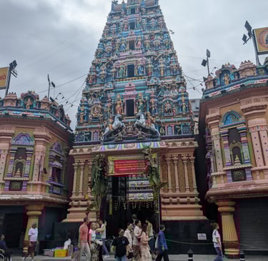 The colorful Dravidian architecture of Sri Mariamman Hindu Temple in Singapore with tourists walking past.