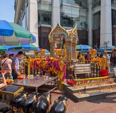 People praying at the Erawan Shrine in Bangkok with flower garlands and incense offerings.