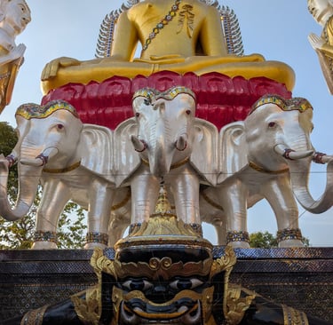 Golden Buddha statue sitting on white elephant sculptures at a Thai temple shrine.