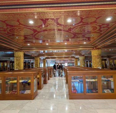 Ornate Buddhist temple interior with red and gold ceilings, showcasing religious texts in glass display cases, and a few