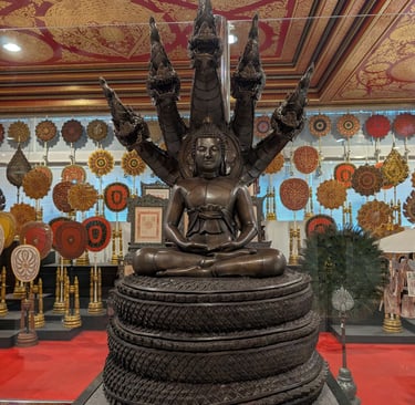 Bronze meditating Buddha statue sheltered by a seven-headed Naga serpent at a Thai temple.