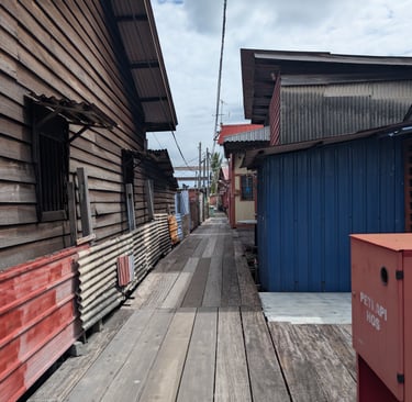 A narrow wooden boardwalk path between traditional rustic houses in a floating stilt village. Yeoh Jetty
