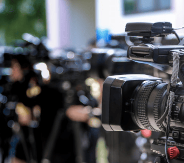 Um cinegrafista aponta sua câmera durante uma entrevista coletiva, no meio de diversos jornalistas.