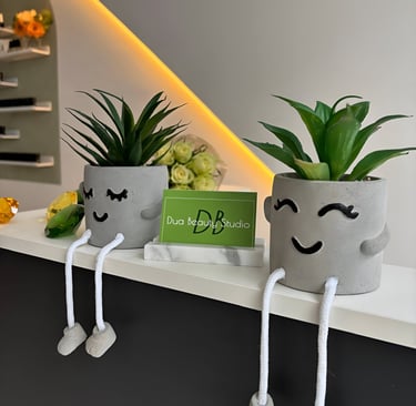 Two plant pots with a smile and a green business card with Dua Beauty Studio on it.