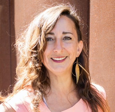 a smiling woman with long hair and golden leaf earrings