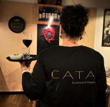 a woman holding a tray with a tray with wine with the CATA logo on the back of the t-shirt