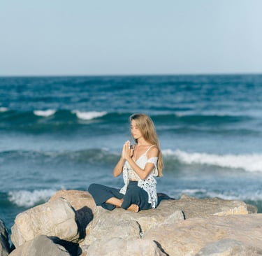 Person meditating on a rock by the ocean, representing emotional regulation and mindfulness Individu