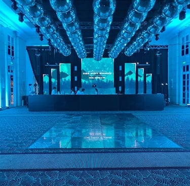 Escenario de evento con pantallas LED verticales, iluminación perimetral azul y pista de baile profe