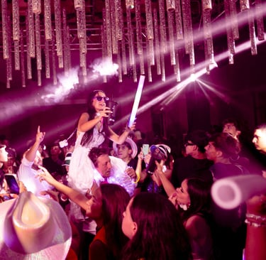 Quinceañera celebrando con sus invitados en pista de baile con luces violetas