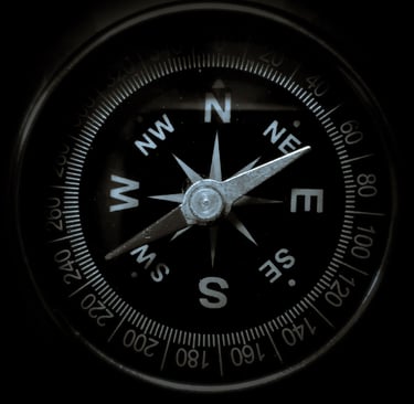 A black compass with a silver needle pointing northeast in a circular frame.