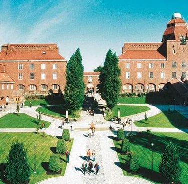 KTH Royal Institute of Technology building with red-tiled roofs, lawn, and trees under a clear blue 