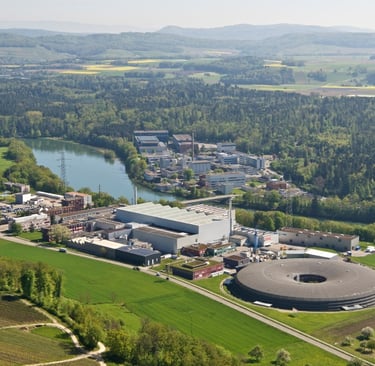 Aerial view of Paul Scherrer Institute complex with verdant landscape, lake, and forested hills