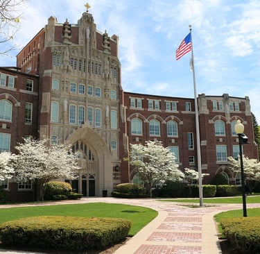 Grand brick building at Providence College with archway, blossoming trees, and American flag