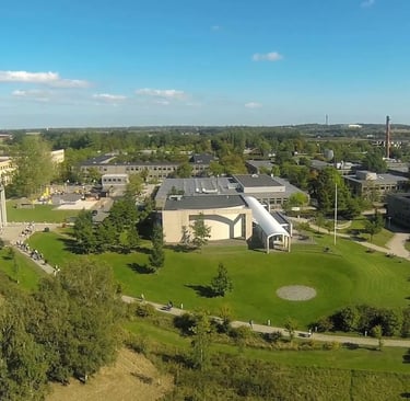 Roskilde University campus aerial view featuring a large building with a curved roof amidst green