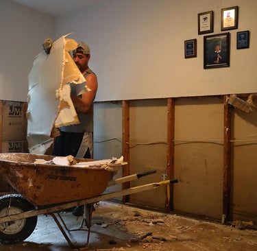 A worker removing damaged drywall debris into a wheelbarrow during a home interior demolition and renovation.