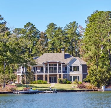 Luxury lakefront home with a private boat dock and manicured lawn surrounded by tall pine trees.