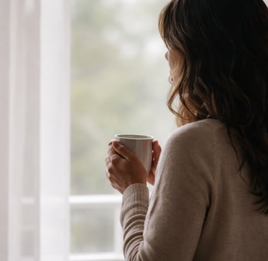 Silueta de mujer mirando por la ventana con una taza de té después de haber perdido su trabajo.