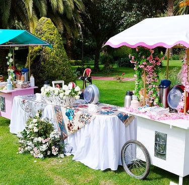 Elegant outdoor garden catering station featuring decorative white and pink beverage carts with floral arrangements.