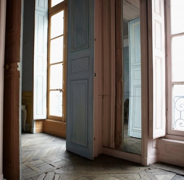 Tall doors standing open in a softly lit Parisian interior, with natural light streaming across aged