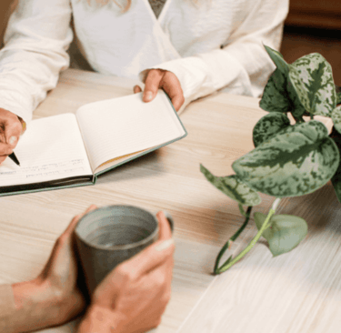 Jacquelien schrijft in haar notitieboek terwijl de klant praat met een kopje koffie in haar hand