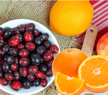 a bowl of cranberries with an oranges and an apple to make fresh cranbery sauce