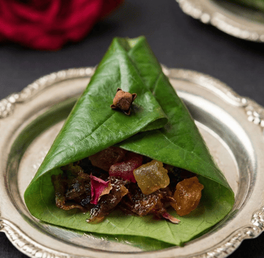 Traditional Indian sweet meetha paan folded in a betel leaf with gulkand and spices on a silver plate.