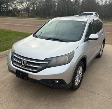Silver Honda CR-V crossover SUV parked on a concrete driveway near a road with trees.