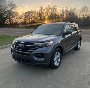 A gray Ford Explorer SUV parked on a concrete lot during a golden hour sunset.