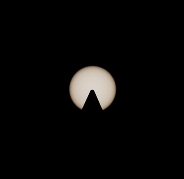 Symmetrical silhouette of an obelisk peak centered against a glowing sun, captured with a solar filter.