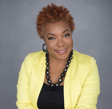 A woman weasring a yellow blazer with a black shirt underneath.  She's wearing a black necklace an d