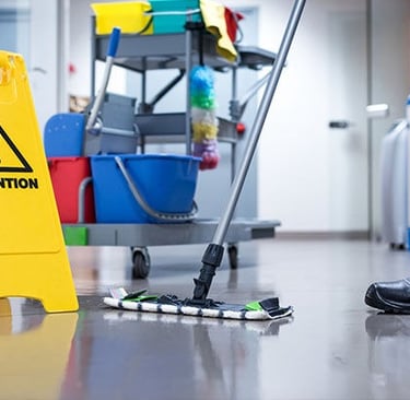 Professional janitor mopping a commercial floor next to a yellow wet floor caution sign.