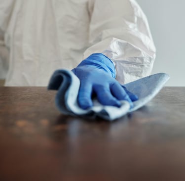 a person in a white lab coat and gloves cleaning a table