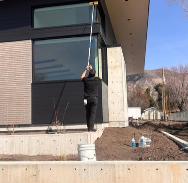 Professional window cleaner using an extension pole on a modern luxury home's exterior glass.