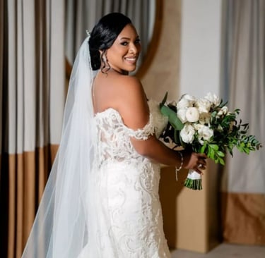 Bride smiling in lace gown with veil and bouquet before her wedding ceremony